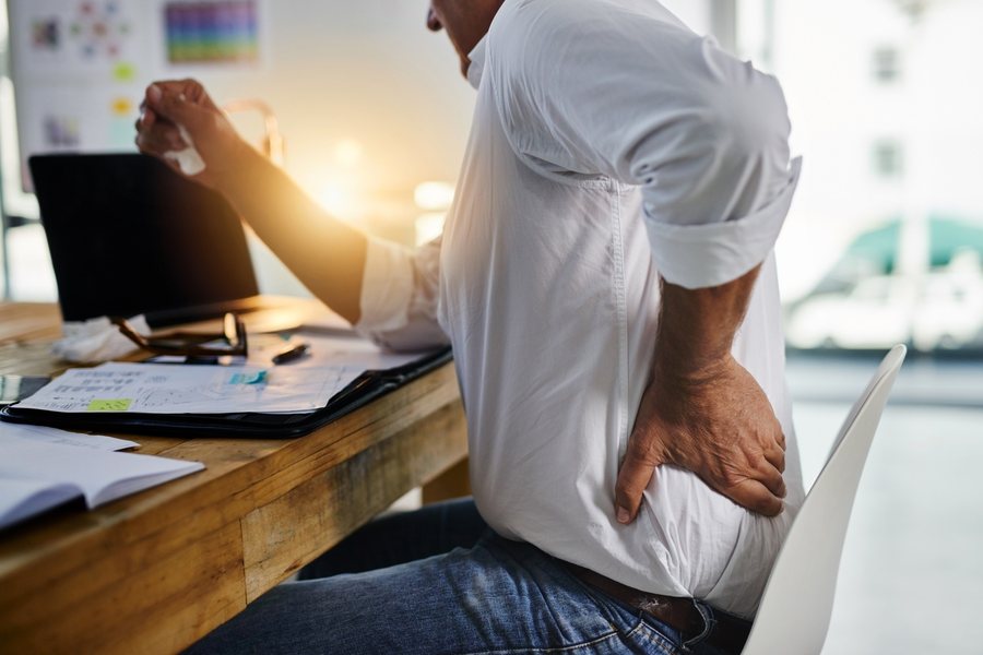 Man at his desk holding his lower back in pain