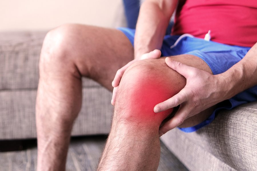 Man sitting on his couch holding his knee in pain
